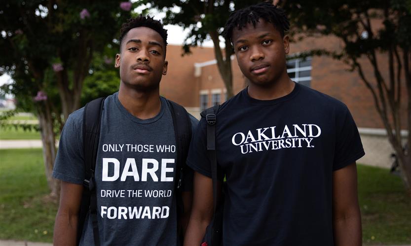 Two students stand in front of their school